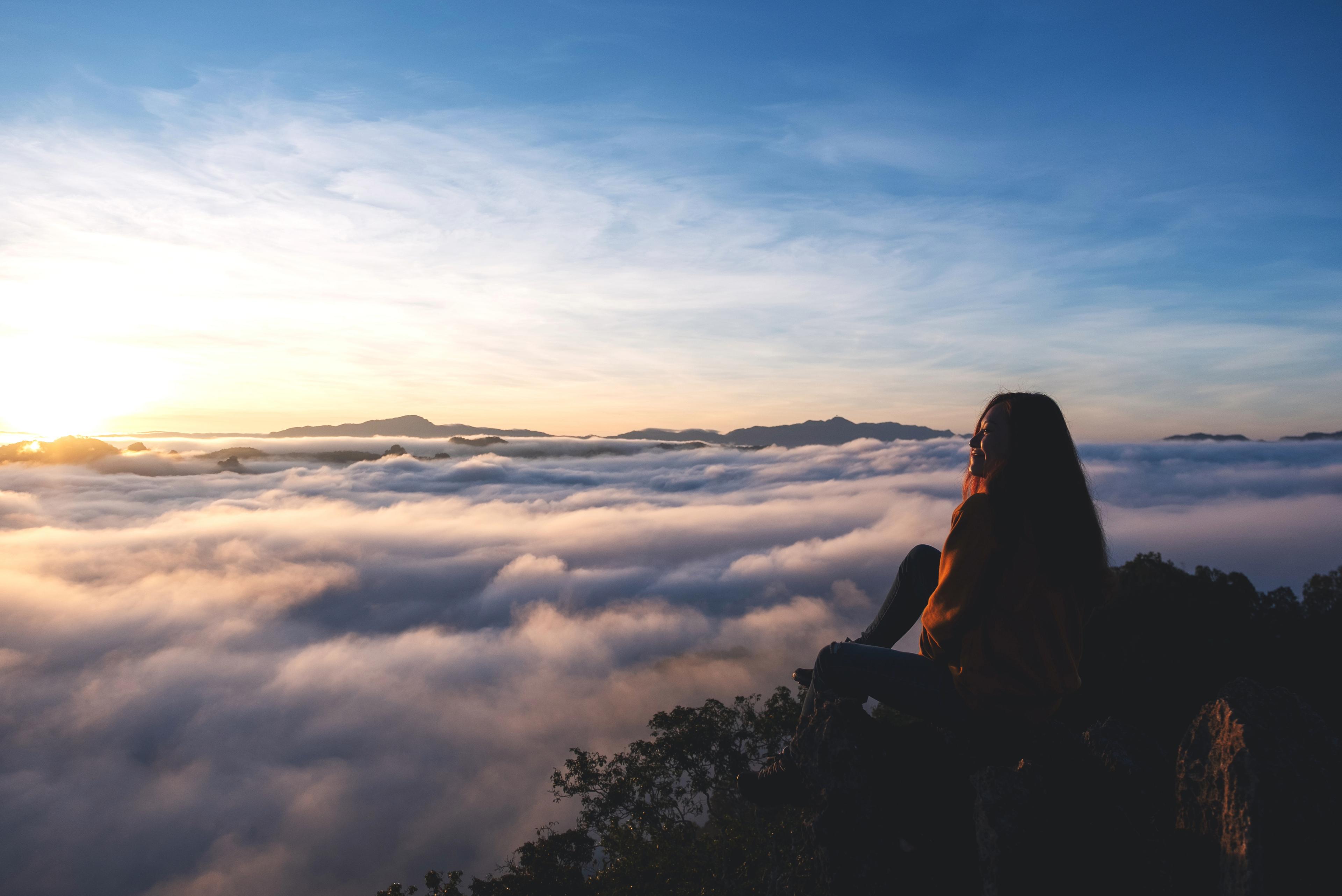 A woman on a mountainside gazes towards the sky, symbolizing a thoughtful perspective on environmental challenges in the aviation sector discussed in the ICAO's Environmental Report